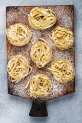 Tagliatelle. Traditional Italian homemade raw uncooked pasta on a wooden Board on a gray concrete background. Selective focus