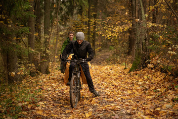 Smiling handsome man in black windbreaker on bicycle in autumn forest