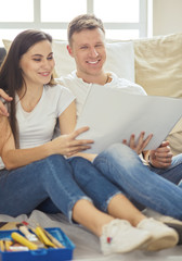 Young couple moving in to new home together, sitting on The floor and diskuss plan of desing.