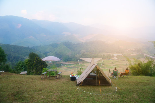 nature camping tent with tree on green grass meadow and mountain in jungle garden with mist on blue sky and people camper sit on chair to family vacation picnic on holiday relax travel in morning warm