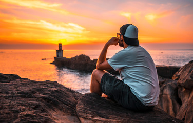 A young man sitting watching the orange sunset of the Pasajes San Juan lighthouse, near San...