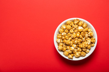 Fototapeta na wymiar Plate with caramel popcorn on a red background, top view. Place for text