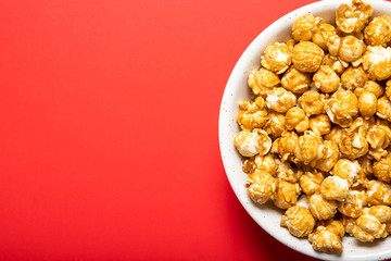 Plate with caramel popcorn on a red background, top view. Place for text