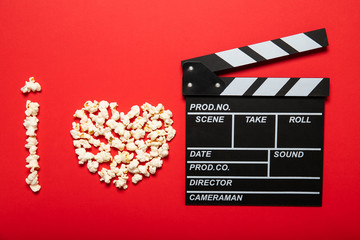 Fototapeta na wymiar Plate with popcorn and movie clapper board on a red background