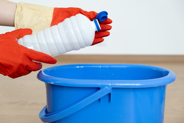  Hands in gloves for cleaning pour a cleaner for cleaning surfaces over a blue bucket.