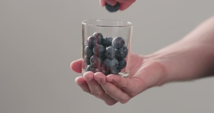 Slow motion man hands take wet washed ripe blueberries from glass jar on neutral background