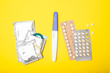 Female hormonal pills, pregnancy test and condoms on a yellow background