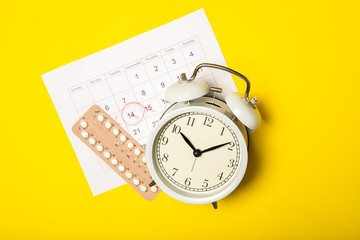 Female birth control pills, calendar and alarm clock on a yellow background. Close-up