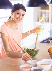 Smiling young woman mixing fresh salad in the kitchen.