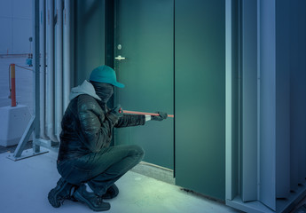 a burglar with a mask and crowbar breaks into a building at night