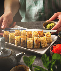a portion sushi rolls on a plate on the table, female hands, close-up