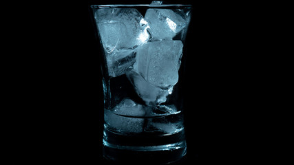 Close-up of melting blue ice cubes in glass with black background