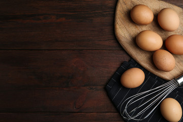 Chicken eggs and whisk on wooden table, flat lay. Space for text
