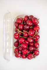 Cherries in open plastic packaging on white background, top view