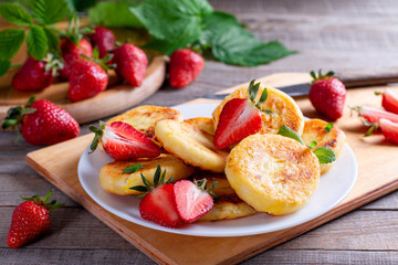 Cottage cheese pancakes or syrniki with sliced strawberry on white plate for breakfast.