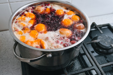 Fresh fruits are boiled in boiling water in a metal pan on the stove. Delicious stewed apricot, apples, cherries, raspberries. Photography, concept.