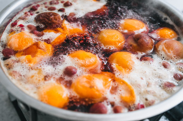 Fresh fruits: apricots, cherries, raspberries, apples are boiled in boiling water in a metal pan on a stove with bubbles and foam close-up. Cooking delicious homemade compote. Photography, concept.