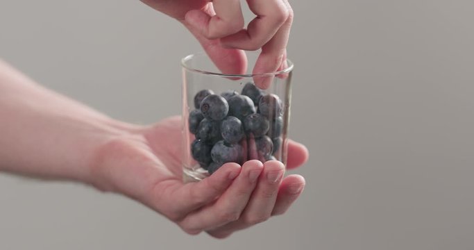 Slow motion man hands take wet washed ripe blueberries from glass jar on neutral background