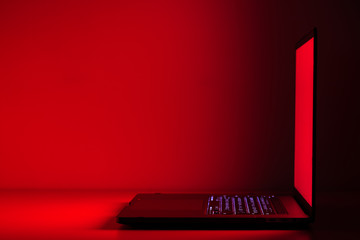 Elegant laptop view in a dark room. Red screen light reflection in dark. 90 degree angle. Side view.