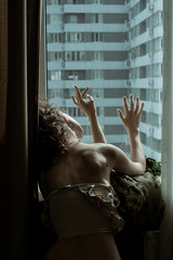 Woman in top touching glass her fingers sitting by a window in flat. Stay isolation at home....