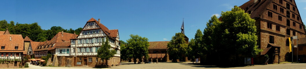 Obraz premium weites Panorama von Klosterkirche in Maulbronn mit Klosterhof und alten Gebäuden unter blauem Himmel