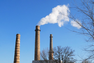 plant tubes with gray smoke on blue sky, chemical plant towers of nuclear power plant against the...