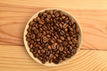 Well-roasted, aromatic coffee grains in a ceramic saucer, on a wooden table.