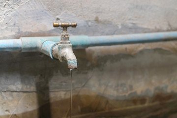 Water from old bass faucet connect to the blue pvc pipe flowing into water surface of bath made of cement close-up.
