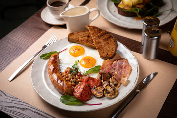 Full English breakfast - fried egg, baked beans, bacon, sausages on a dark rusty background, toasts.