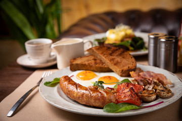 Full English breakfast - fried egg, baked beans, bacon, sausages on a dark rusty background, toasts.