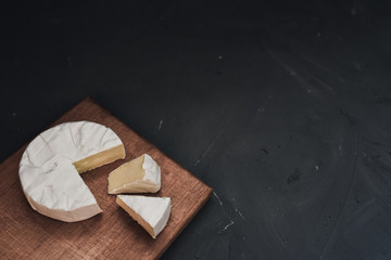 Camembert round cheese and a slice lie on a wooden board. grey matte concrete background.