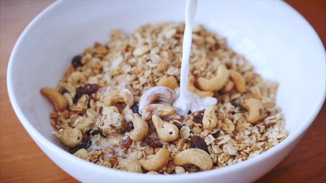 The concept of breakfast, a healthy diet, granola with cashew nuts and slices of raspberries and raisins. Slow motion milk pouring in bowl of muesli breakfast cereals. Healthy food
