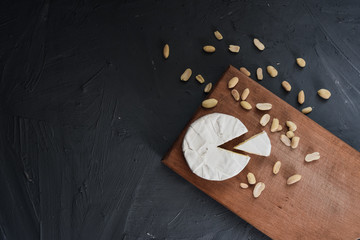 Camembert round cheese and a slice lie on a wooden board. grey matte concrete background. peanut