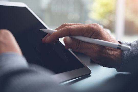 Closeup of man hand with stylus pen using digital tablet computer on table at home office