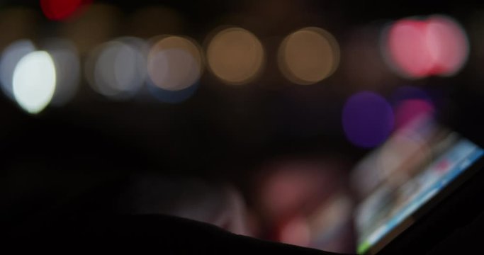 Person using digital tablet device at night with city lights in background - out of focus blurry concept footage
