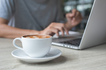 Casual business man surfing the internet while online working on laptop computer with cup of coffee on table in coffee shop