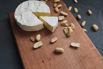 Camembert round cheese and a slice lie on a wooden board. grey matte concrete background. peanut