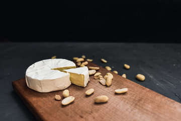 Camembert round cheese and a slice lie on a wooden board. grey matte concrete background. peanut