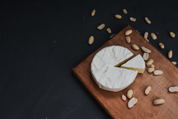 Camembert round cheese and a slice lie on a wooden board. grey matte concrete background. peanut