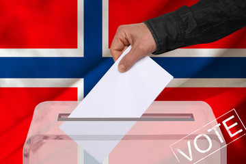 male voter drops a ballot in a transparent ballot box against the background of the national flag...