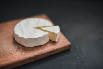 Camembert round cheese and a slice lie on a wooden board. grey matte concrete background.