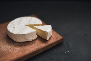 Camembert round cheese and a slice lie on a wooden board. grey matte concrete background.