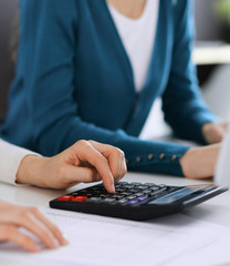 Accountant checking financial statement or counting by calculator income for tax form, hands closeup. Business woman sitting and working with colleague at the desk in office toned in blue. Tax and