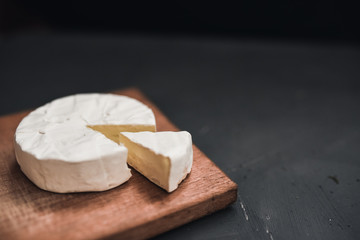 Camembert round cheese and a slice lie on a wooden board. grey matte concrete background.
