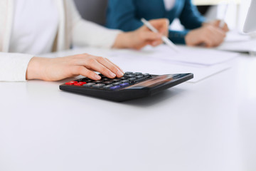 Obraz na płótnie Canvas Accountant checking financial statement or counting by calculator income for tax form, hands closeup. Business woman sitting and working with colleague at the desk in office toned in blue. Tax and