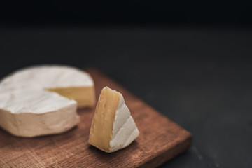 Camembert round cheese and a slice lie on a wooden board. grey matte concrete background.