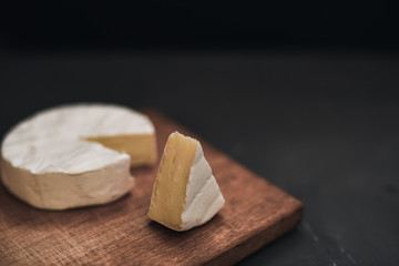 Camembert round cheese and a slice lie on a wooden board. grey matte concrete background.