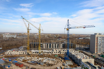 Fototapeta na wymiar Photos of high-rise construction cranes and an unfinished house against a blue sky. Top view of the construction site.