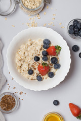 Oatmeal porridge with strawberry, blueberry, flax seeds and honey on gray background.