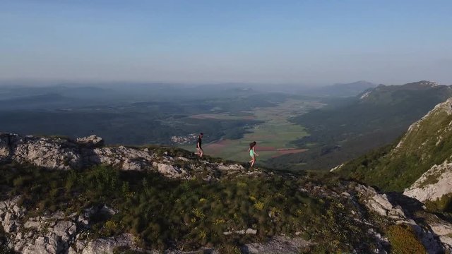 A couple running down a slope at the top of a mountain with beautiful and amazing lands at the back teasing the new normality and enjoying after the lockdown